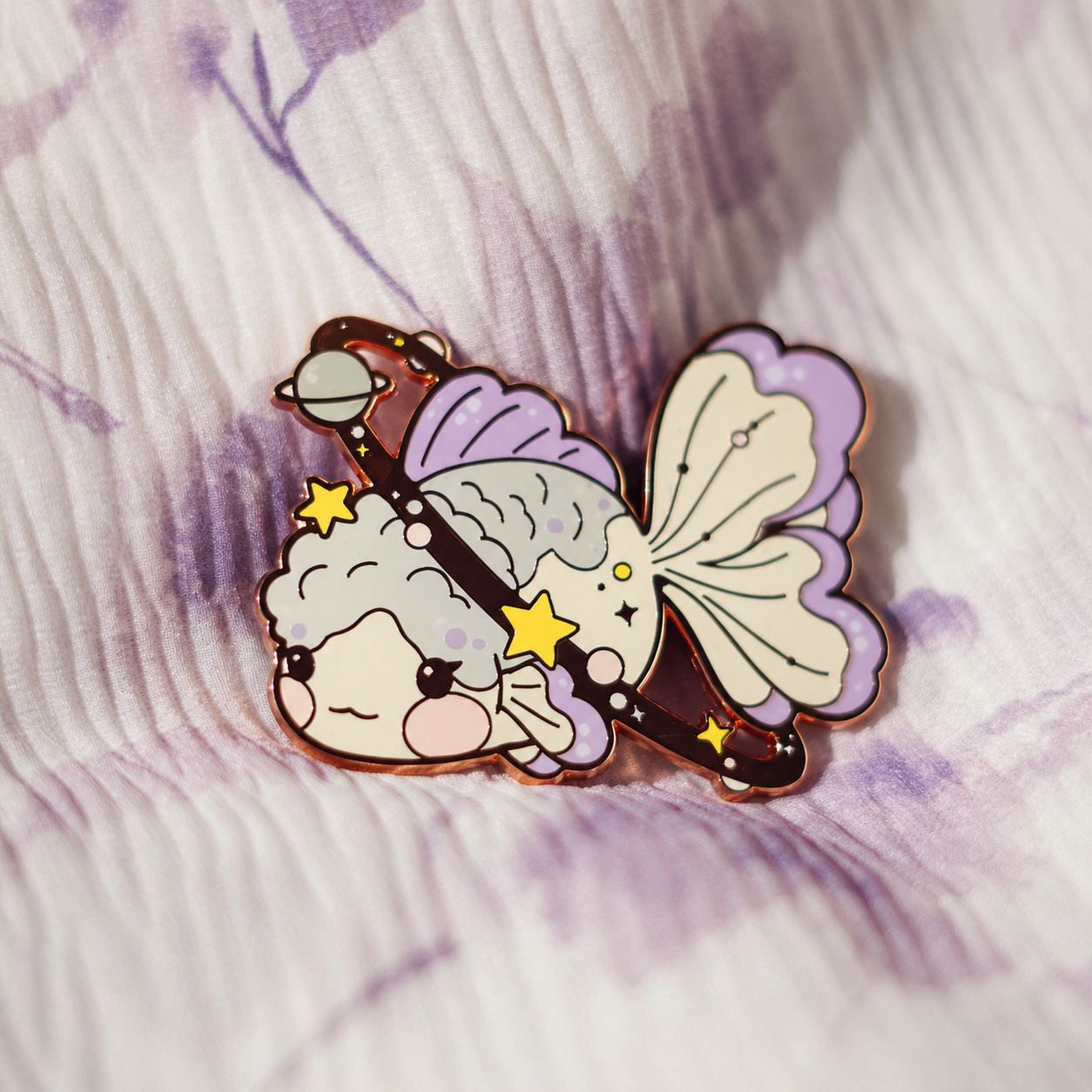 Pastel goldfish enamel pin with stars and a planet motif; enhanced photograph of the finished product