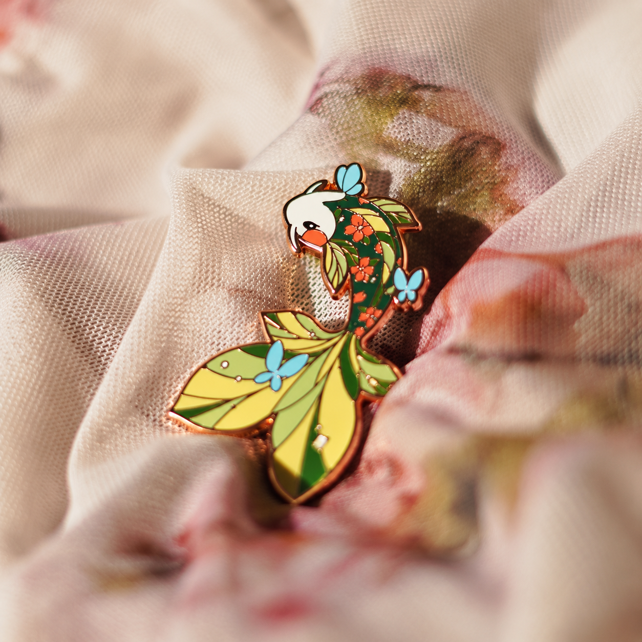 Green koi enamel pin with leaves and blossoms; enhanced photograph of the finished product